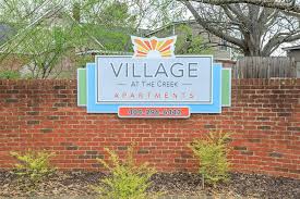 A sign for Village at the Creek Apartments is displayed on a brick wall.
